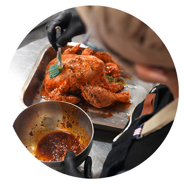Cocinera untando salsa casera sobre un pollo asado de Miss Croquette antes del horneado.